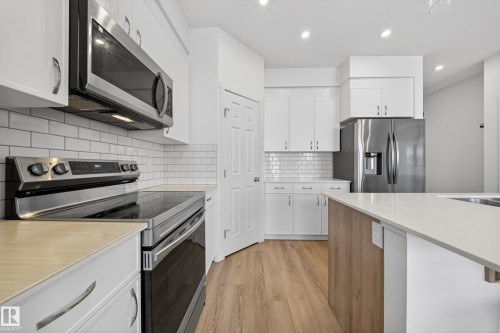 Contemporary kitchen featuring white cabinetry, stainless steel appliances, a subway tile backsplash, and light wood-finish flooring - 1684 12 Street, Edmonton, AB 
