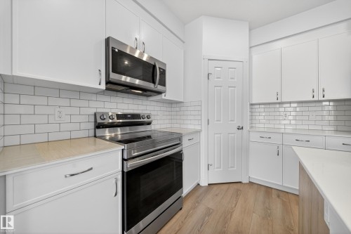 Kitchen featuring white cabinetry, stainless steel appliances, wood-finish flooring, white subway tile backsplash, and light-toned countertops - 1684 12 Street, Edmonton, AB 