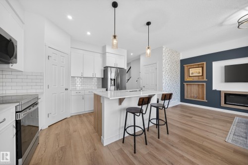 Open-concept kitchen and living area featuring white cabinetry, subway tile backsplash, stainless steel appliances, a kitchen island with seating, and wood-finish flooring - 1684 12 Street, Edmonton, AB 