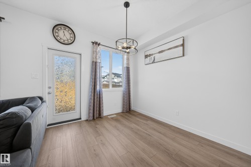 Open-concept living area featuring wood-finish flooring, a contemporary black pendant light fixture, and multiple windows for abundant natural light - 1684 12 Street, Edmonton, AB 