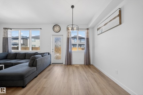 Open-concept living area featuring wood-finish flooring, white walls, and a contemporary black metal chandelier - 1684 12 Street, Edmonton, AB 