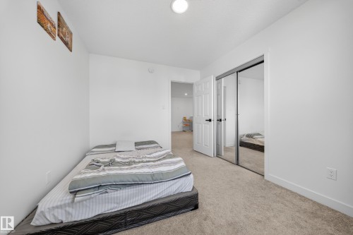 Bright interior space featuring light neutral carpeting, white baseboards, and a mirrored sliding closet door - 1684 12 Street, Edmonton, AB 