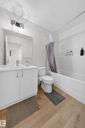 Bathroom featuring a single vanity with built-in storage, a wall-mounted mirror, modern light fixture, and a tub-shower combination with subway tile surround - 1684 12 Street, Edmonton, AB 