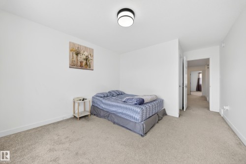 Bright bedroom featuring neutral carpeting, white walls, a flush-mount ceiling light fixture, and white baseboards - 1684 12 Street, Edmonton, AB 