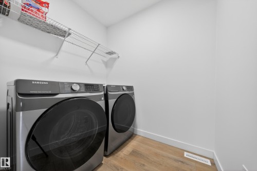 Dedicated laundry area featuring wood-finish flooring, a wall-mounted wire shelving unit, and painted baseboards - 1684 12 Street, Edmonton, AB 