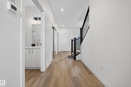 Entryway featuring wood-finish flooring, recessed lighting, and a contemporary black metal staircase railing - 1684 12 Street, Edmonton, AB 