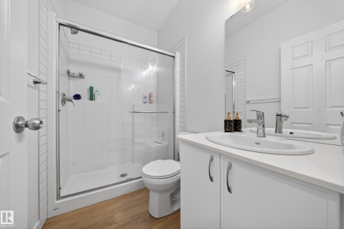 Bathroom featuring a glass-enclosed shower, white vanity with integrated sink, chrome fixtures, wood-finish flooring, and a large wall mirror - 1684 12 Street, Edmonton, AB 