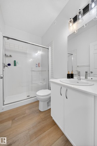 Bathroom featuring a glass-enclosed shower, white vanity with integrated sink, wood-finish flooring, and subway tile accent wall - 1684 12 Street, Edmonton, AB 