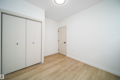 Interior room featuring wood-finish flooring, white walls, and a contemporary flush-mount ceiling light - 10866 92 Street, Edmonton, AB 