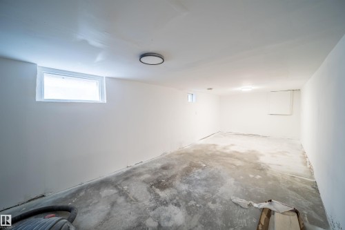 Spacious lower level room featuring a white ceiling, light-colored walls, flush-mount lighting, and an egress window - 10866 92 Street, Edmonton, AB 