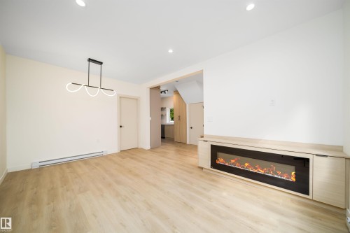 Spacious room featuring light wood-finish flooring, a contemporary linear chandelier, and recessed lighting - 10866 92 Street, Edmonton, AB 