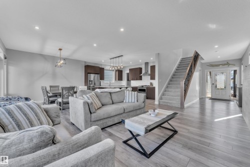 Spacious open-concept living area featuring wood-finish flooring, recessed lighting, and a modern staircase with dark wood banister - 17551 64 Street, Edmonton, AB 