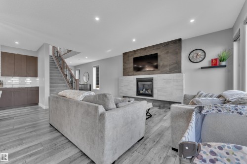 Open-concept living area featuring wood-finish flooring, a contemporary fireplace with a tiled surround, recessed lighting, and a staircase with metal balusters - 17551 64 Street, Edmonton, AB 