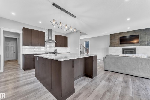 Spacious kitchen island with light-toned countertop, complemented by dark wood-finish cabinetry, subway tile backsplash, and a stainless steel range hood - 17551 64 Street, Edmonton, AB 