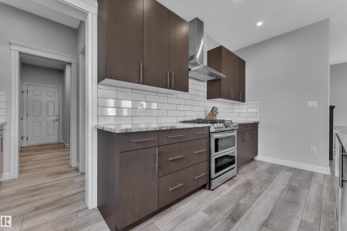 Kitchen featuring dark wood-finish cabinetry, light-toned countertops, a subway tile backsplash, a stainless steel range with a double oven, and wood-finish flooring - 17551 64 Street, Edmonton, AB 