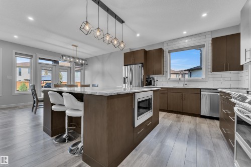 Modern kitchen featuring a large island with a light-toned countertop, integrated microwave, and pendant lighting - 17551 64 Street, Edmonton, AB 