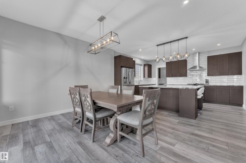 Open-concept dining and kitchen area featuring wood-finish flooring, recessed lighting, and a linear chandelier - 17551 64 Street, Edmonton, AB 