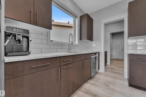 Contemporary kitchen featuring brown cabinetry, light-toned countertops, and a white subway tile backsplash - 17551 64 Street, Edmonton, AB 