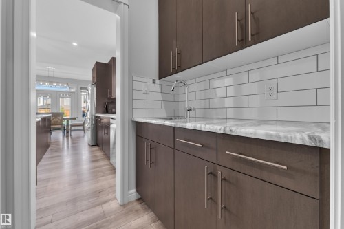 Kitchenette featuring rich brown cabinetry with brushed nickel hardware, a marble-patterned countertop, a stainless steel faucet, and a subway tile backsplash - 17551 64 Street, Edmonton, AB 