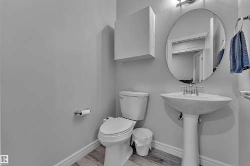 Powder room featuring a pedestal sink, oval mirror, and wood-finish flooring - 17551 64 Street, Edmonton, AB 