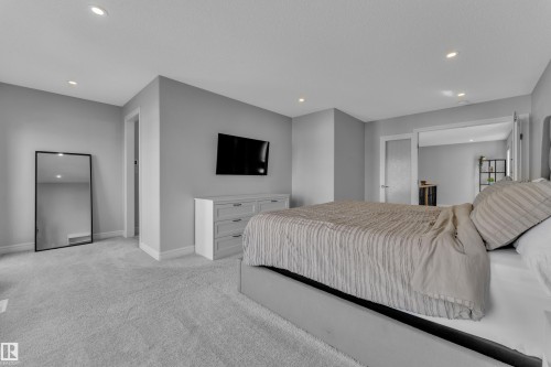Spacious bedroom featuring light gray walls, recessed ceiling lighting, light gray carpet, white baseboards, and a frosted glass panel door - 17551 64 Street, Edmonton, AB 