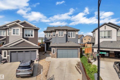 Two-story residence featuring a gray exterior with stone accents, a two-car garage, and a concrete driveway - 17551 64 Street, Edmonton, AB 