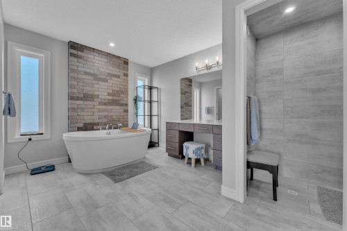 Freestanding soaking tub with a stone accent wall, dual windows, spacious vanity with integrated sink, and a separate walk-in shower with tiled walls and recessed lighting - 17551 64 Street, Edmonton, AB 