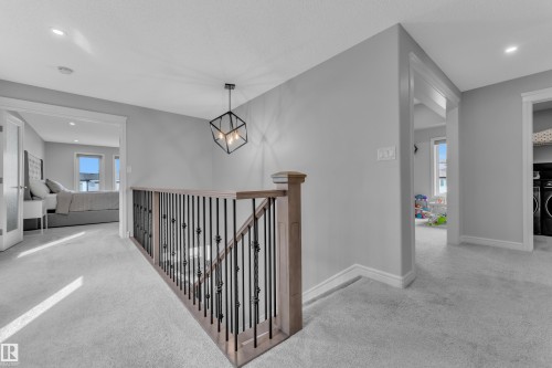 Staircase featuring wood-finish handrail and black wrought iron balusters under a contemporary geometric pendant light - 17551 64 Street, Edmonton, AB 