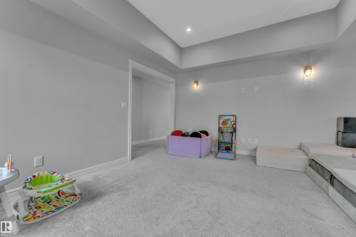 Spacious carpeted room featuring recessed lighting and wall sconces, neutral gray wall finish, and white baseboards - 17551 64 Street, Edmonton, AB 