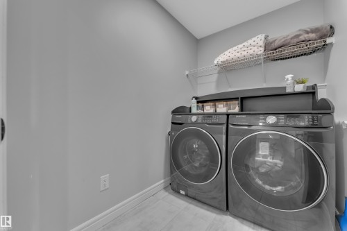 Dedicated laundry area featuring front-loading appliances, a built-in wire shelf, and light-toned flooring - 17551 64 Street, Edmonton, AB 