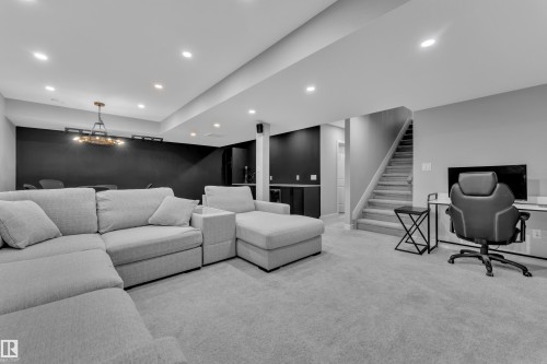 Spacious lower level featuring recessed lighting, a modern chandelier, plush carpeting, and a built-in bar area - 17551 64 Street, Edmonton, AB 