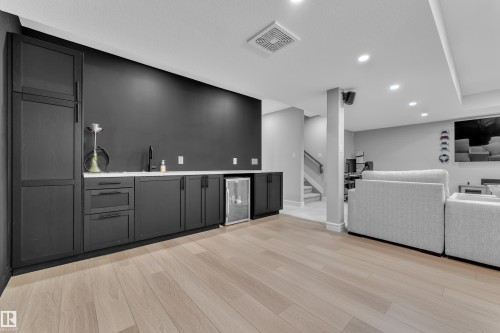 Lower-level entertainment space featuring a wet bar with dark cabinetry, integrated sink, and beverage refrigerator - 17551 64 Street, Edmonton, AB 