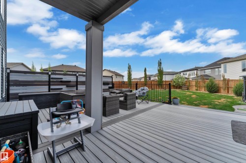 Expansive composite deck featuring a privacy wall with integrated lighting, a covered patio area, and direct access to the manicured lawn - 17551 64 Street, Edmonton, AB 