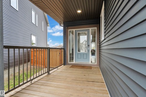 Covered front porch with wood-finish decking, black metal railings, and a light blue entry door with decorative glass inserts - 17551 64 Street, Edmonton, AB 