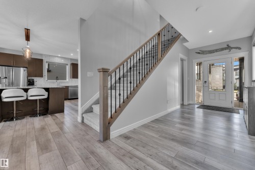 Open-concept entryway featuring light wood-finish flooring, a carpeted staircase with a wood handrail and wrought iron spindles, a white paneled front door with sidelight windows, and recessed lighting - 17551 64 Street, Edmonton, AB 