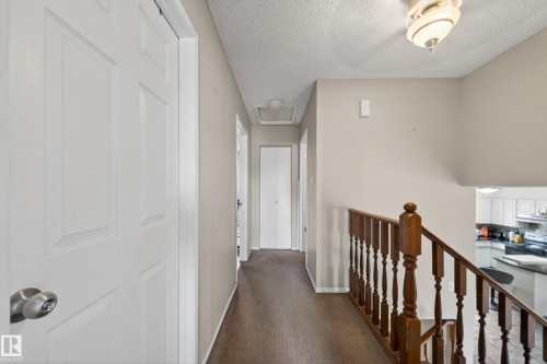 Hallway featuring a textured ceiling, a wood-finish handrail, and white paneled doors - 2832 35 Street, Edmonton, AB 