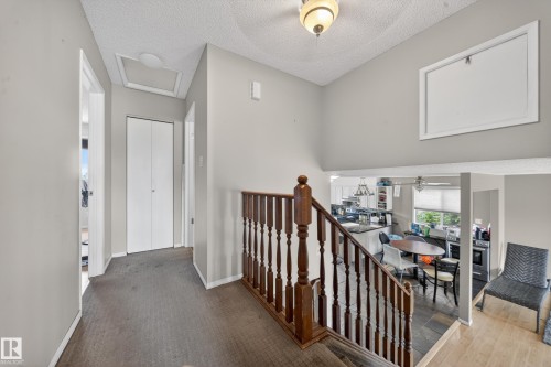 Upper-level hallway with neutral wall paint and textured ceiling, featuring a wood-finish staircase railing and carpeted flooring - 2832 35 Street, Edmonton, AB 