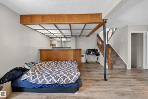 Spacious room featuring wood-finish flooring, light grey painted walls, and a wood-paneled drop ceiling with integrated lighting - 2832 35 Street, Edmonton, AB 