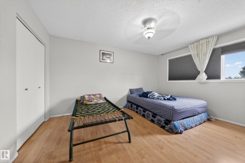 Bedroom featuring wood-finish flooring, light grey walls, white bi-fold closet doors, a window with a roller shade and sheer curtain, and a ceiling-mounted light fixture - 2832 35 Street, Edmonton, AB 