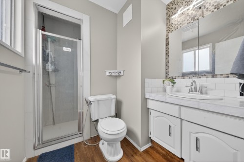 Bathroom featuring a glass-enclosed shower, white vanity with an undermount sink, marble-finish countertop, and a mosaic tile accent wall - 2832 35 Street, Edmonton, AB 