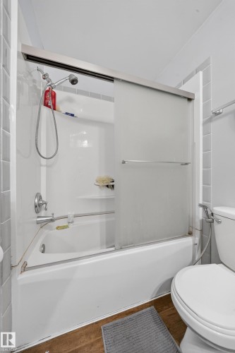 Bathroom featuring a white bathtub with a sliding frosted glass shower door, chrome fixtures, and white subway tile surround - 2832 35 Street, Edmonton, AB 