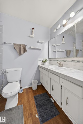 Bathroom featuring wood-finish flooring, a white vanity with a single sink, an overhead vanity light fixture, and a wall-mounted medicine cabinet with mirror - 2832 35 Street, Edmonton, AB 