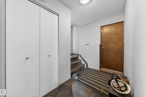 Foyer featuring slate tile flooring, wood-finish interior door, textured ceiling, and bi-fold closet doors - 2832 35 Street, Edmonton, AB 