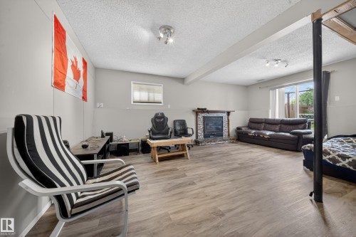 Spacious interior featuring wood-finish flooring, a stone-surround fireplace with a wood mantel, a sliding glass door, and recessed lighting - 2832 35 Street, Edmonton, AB 