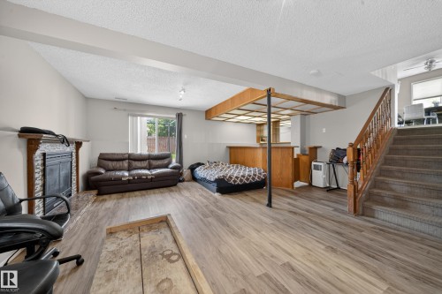 Spacious lower-level area featuring wood-finish flooring, a fireplace with stone tile surround and wood mantel, a built-in wet bar with wood cabinetry, and a carpeted staircase with wood banister - 2832 35 Street, Edmonton, AB 