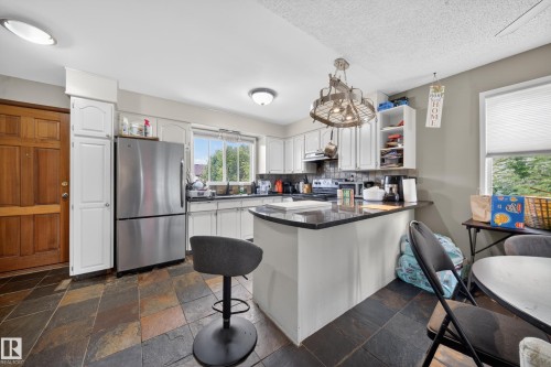 Kitchen featuring multi-toned slate tile flooring, white cabinetry, dark countertops, and a stainless steel refrigerator - 2832 35 Street, Edmonton, AB 