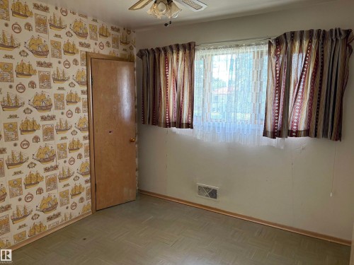 Room featuring patterned wallpaper, a window with sheer and patterned curtains, a ceiling fan, a wood-finish door, and patterned floor tiles - 5511 50 St, Tofield, AB 