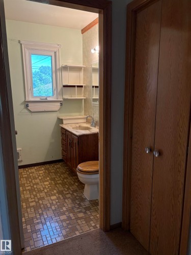 Bathroom featuring a window, built-in wall shelving, a vanity with a counter and integrated sink, a wall-mounted light fixture, and patterned flooring - 5511 50 St, Tofield, AB 