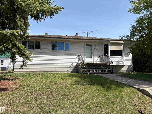 Single-story residence featuring white horizontal siding, a gabled roof, and a front entry with metal railings - 5511 50 St, Tofield, AB 