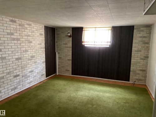 Interior room featuring white painted brick walls, dark wood paneling, green carpet flooring, and a drop ceiling - 5511 50 St, Tofield, AB 